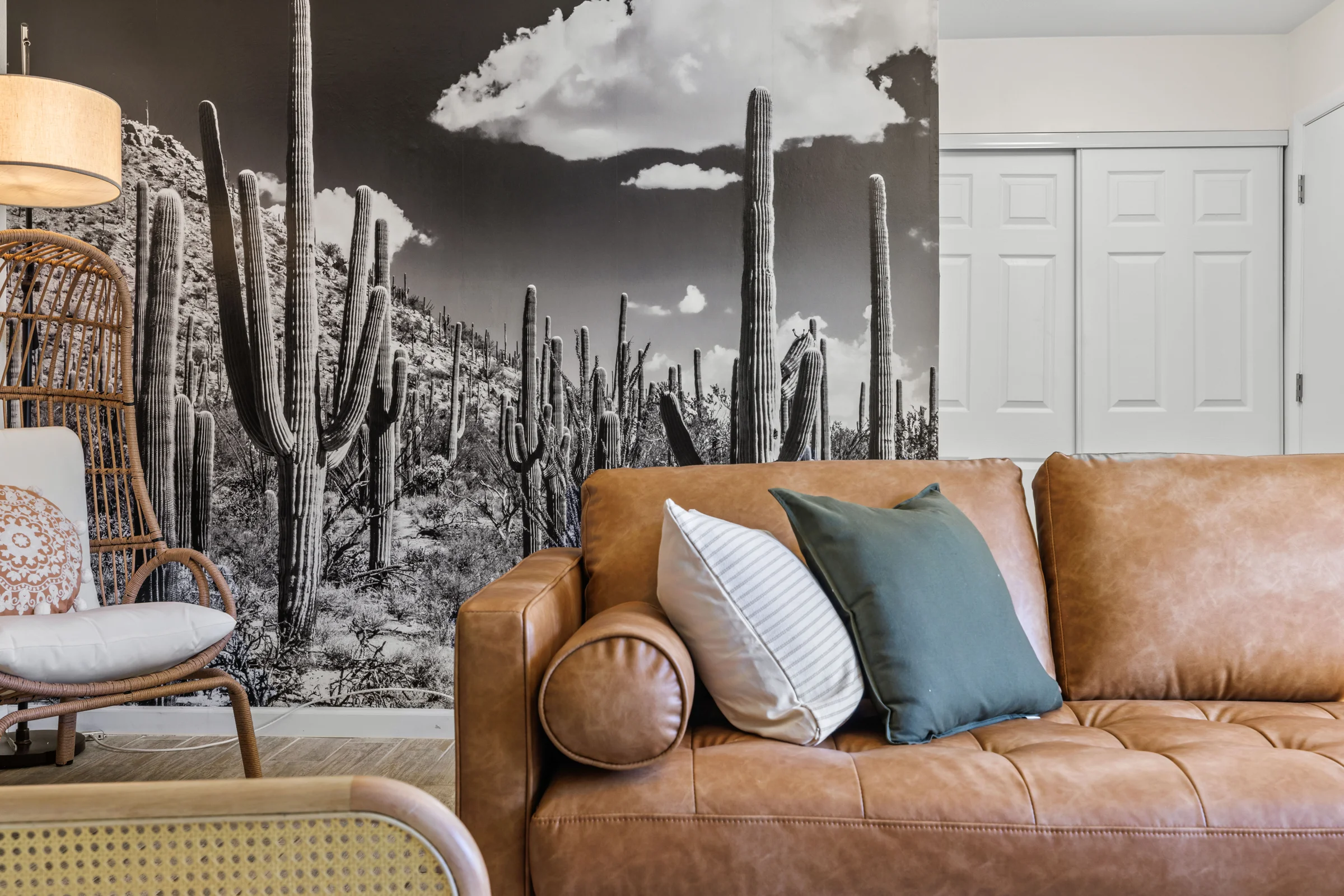 Stylish living room featuring a tan leather sofa with accent pillows, a wicker chair, and a striking black-and-white cactus wall mural.