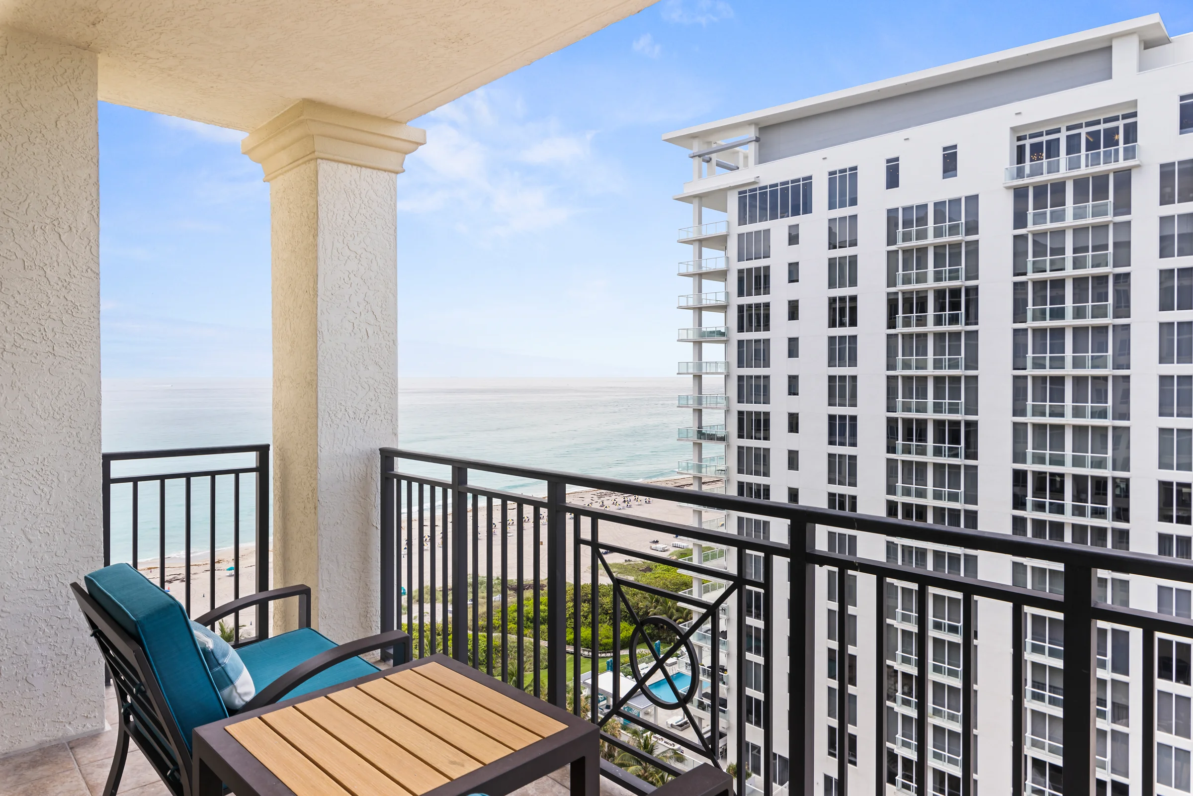 Balcony with outdoor seating overlooking a beach and modern high-rise building.