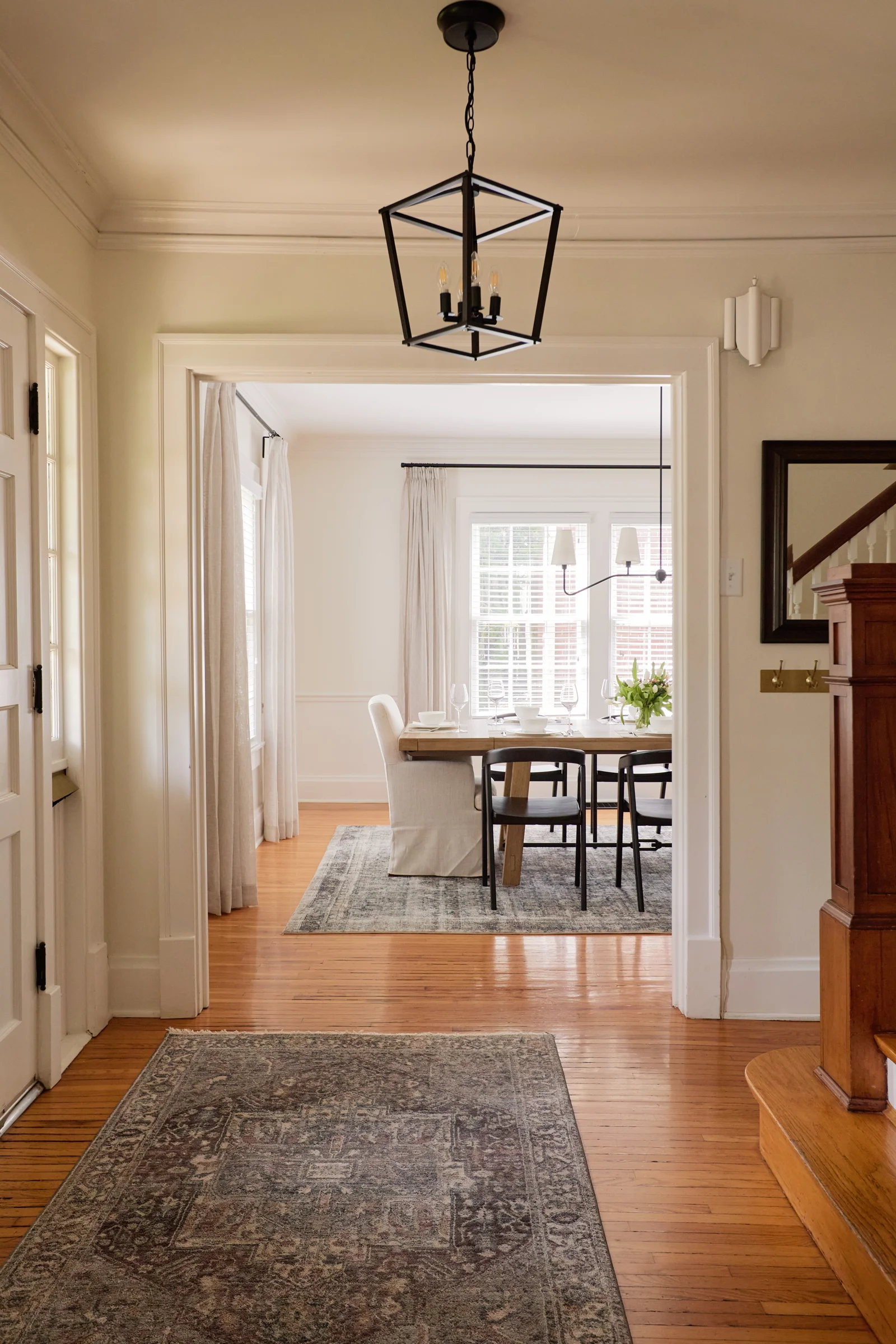 A view of a warm and inviting dining area through a hallway, featuring a vintage rug, wooden floors, and natural light flowing through large windows.