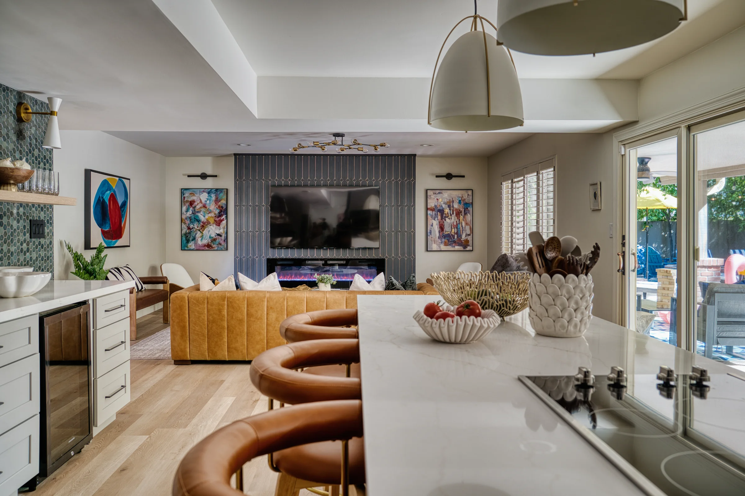 Modern open-concept kitchen and living area featuring a stylish island with leather barstools, a cozy seating area, and a decorative fireplace. Photographed by Shane Baker Studios.