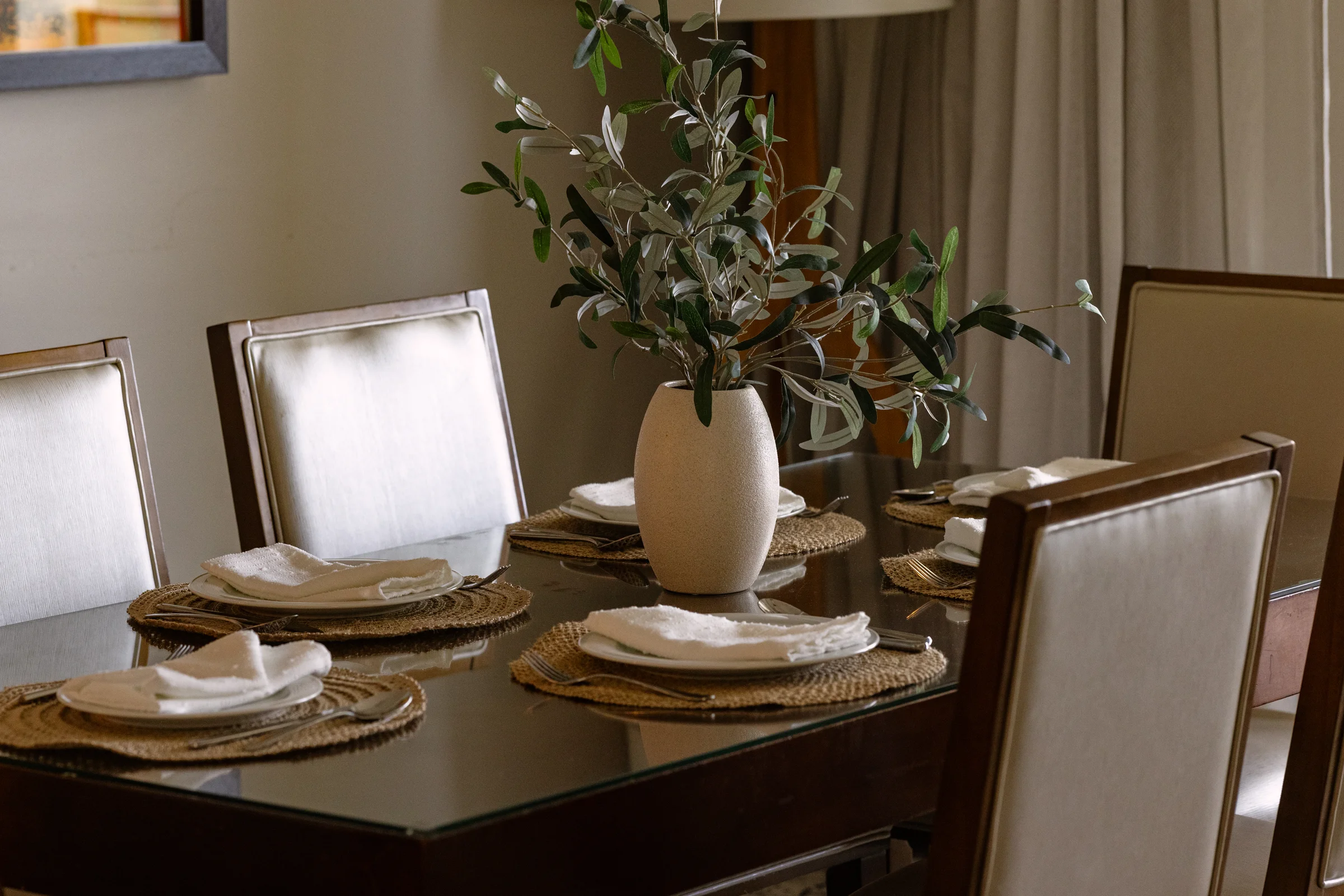 Elegant dining table setup with a centerpiece vase holding leafy branches and neatly arranged place settings.