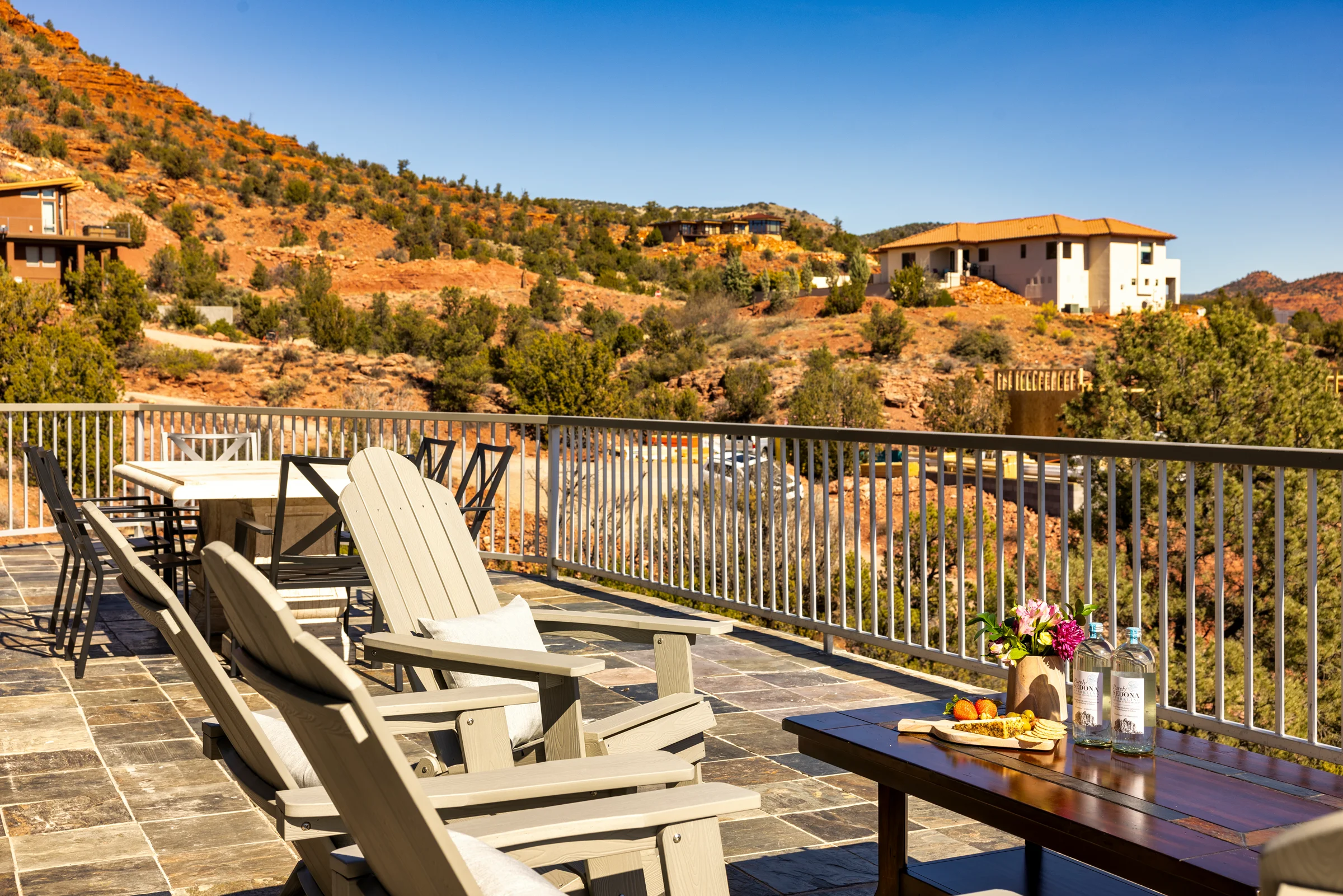 Elevated patio with Adirondack chairs and a dining table overlooking the stunning Sedona red rock landscape. Photographed by Shane Baker Studios.