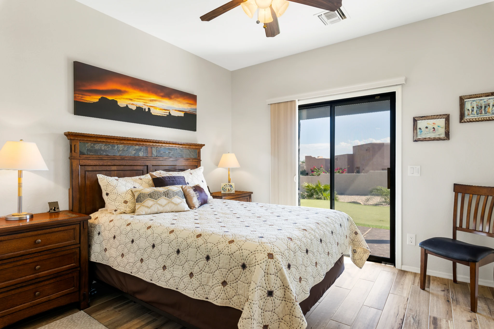 A cozy Southwestern-style bedroom with a wooden bed frame, warm lighting, and a sliding glass door leading to a landscaped backyard. Photographed by Shane Baker Studios.