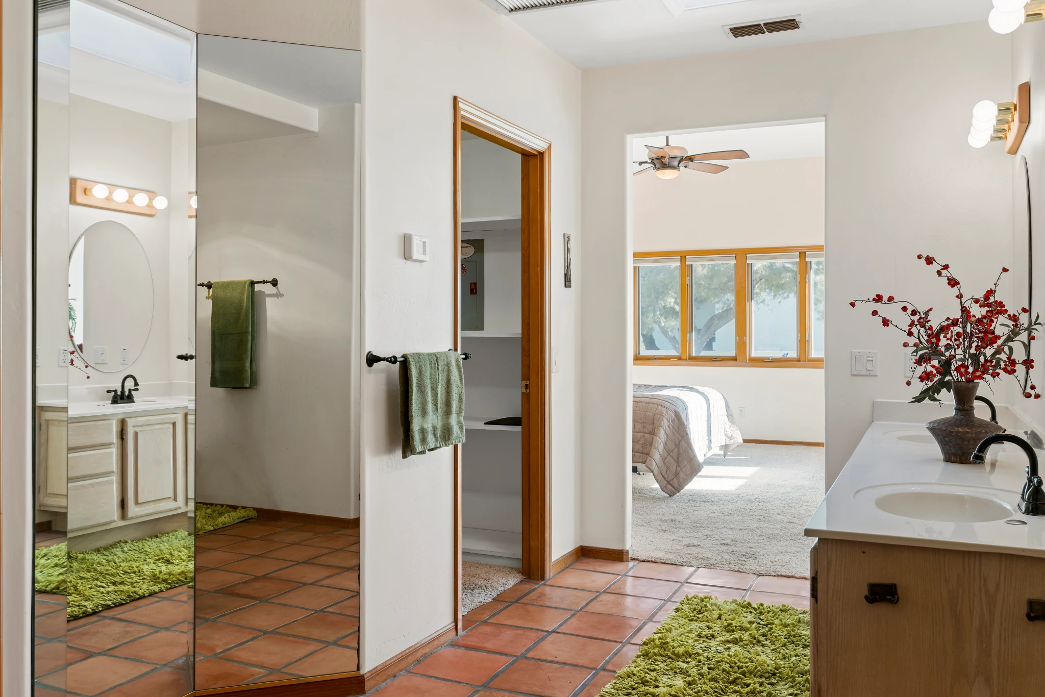 A Southwestern-style bathroom with terracotta tile flooring, a double vanity, and a large mirror, leading into a bright bedroom. Photographed by Shane Baker Studios.