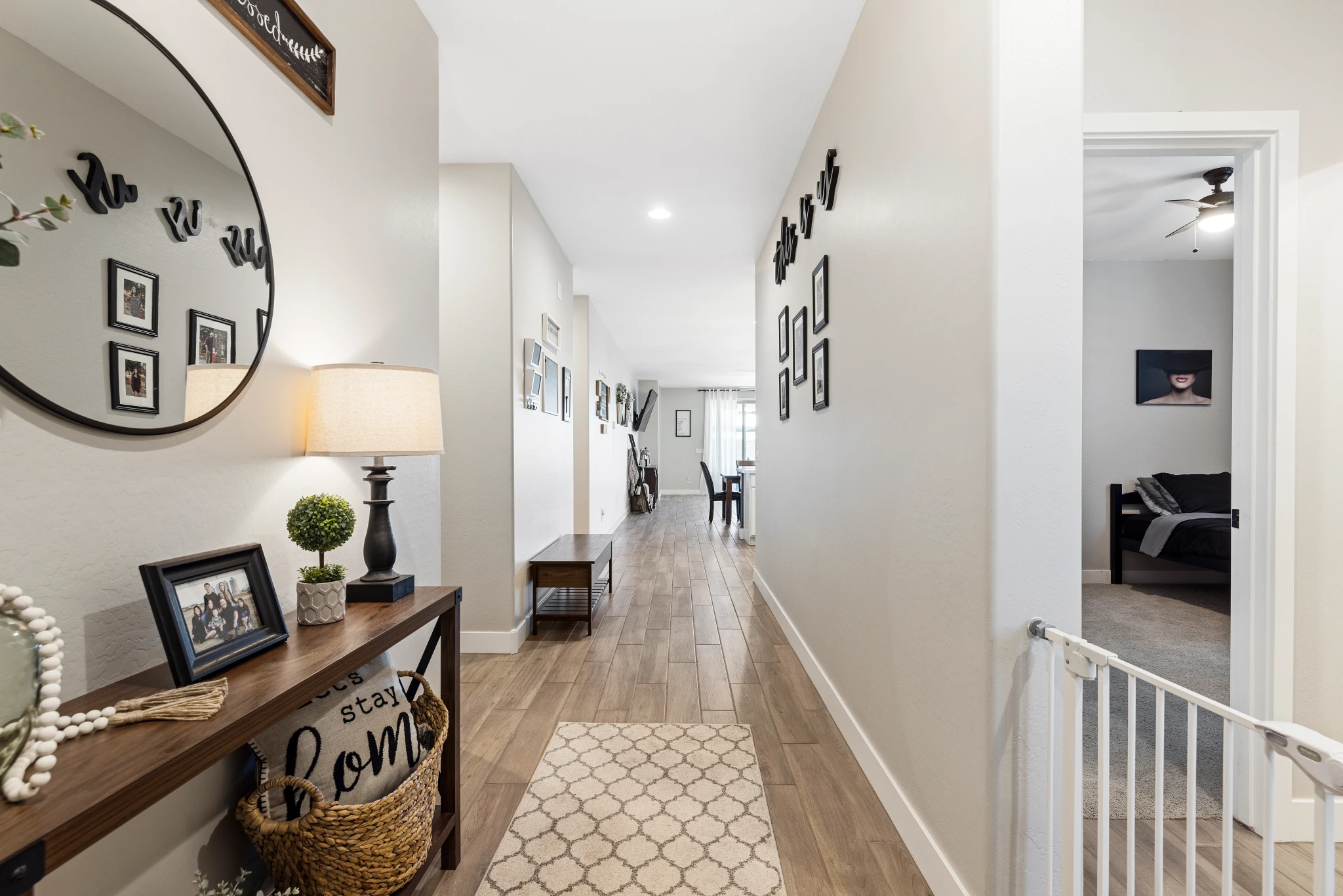 A well-lit hallway with wood-look tile flooring, stylish decor, and a glimpse into a bedroom. Photographed by Shane Baker Studios.