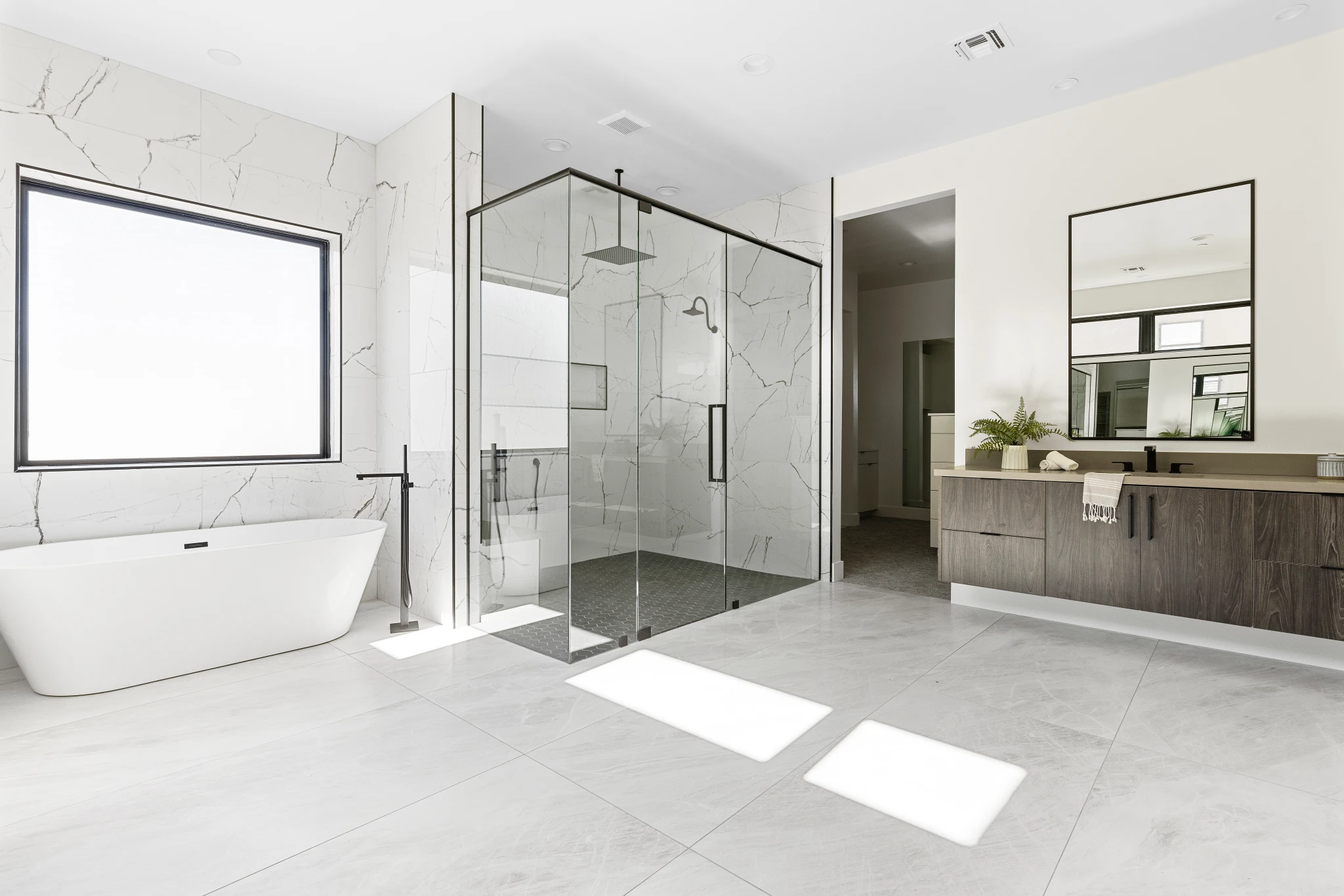 A modern primary bathroom featuring a glass-enclosed shower, freestanding soaking tub, and sleek floating vanity with a large mirror. Photographed by Shane Baker Studios.