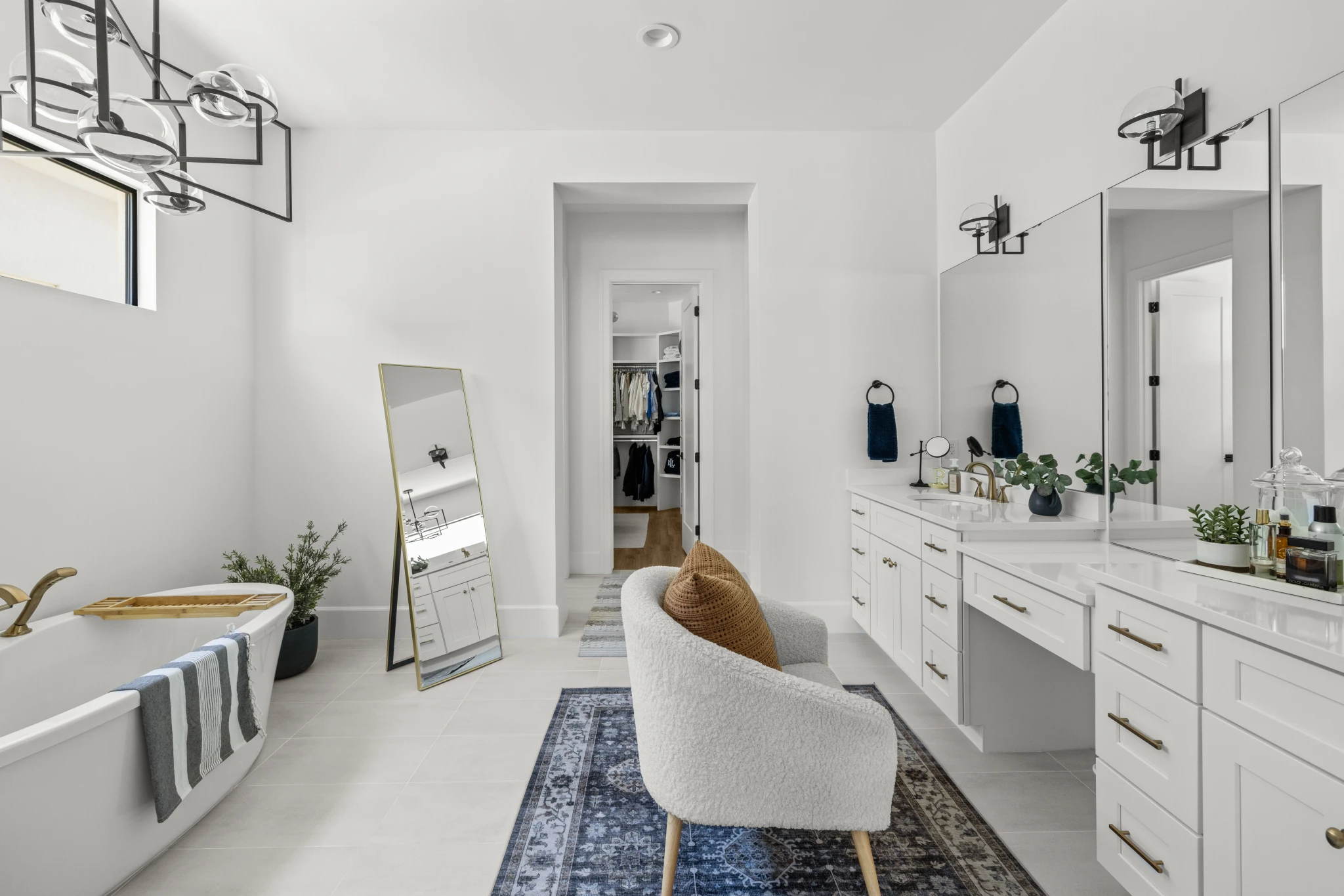 A luxurious modern bathroom featuring a freestanding tub, double vanity, elegant lighting, and a stylish seating area. Photographed by Shane Baker Studios.