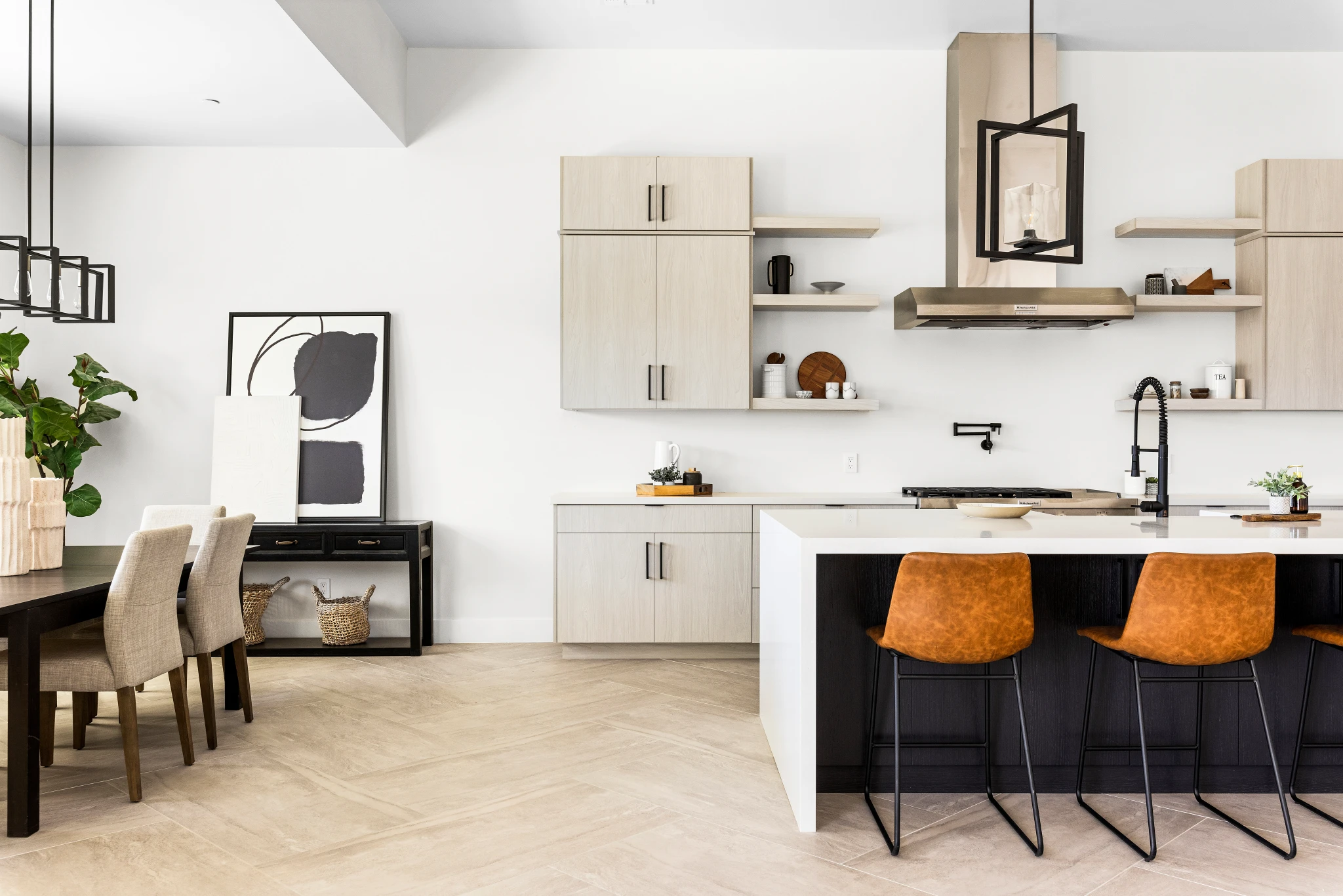 A modern kitchen and dining area featuring sleek cabinetry, a spacious island with leather barstools, and elegant decor. Photographed by Shane Baker Studios.