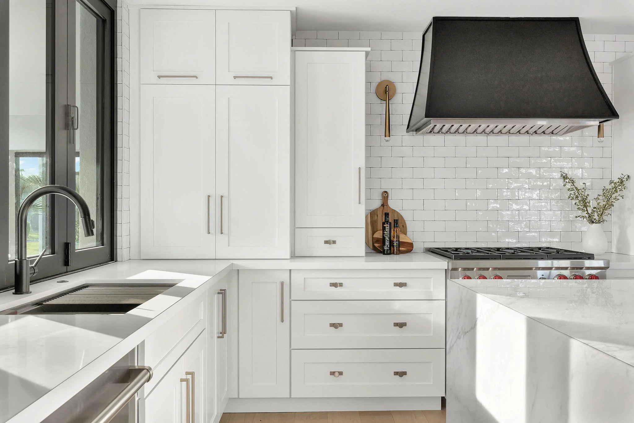 Modern white kitchen with subway tile backsplash, black range hood, and a sleek sink design.