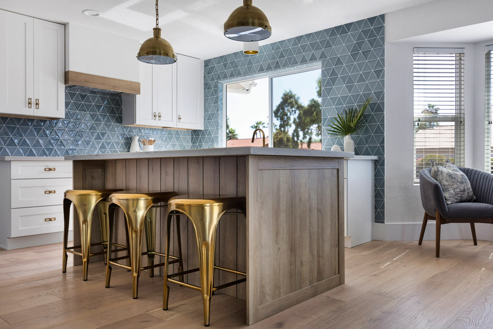 Modern kitchen design with a blue geometric tile backsplash, wood-paneled island, gold barstools, and brass pendant lighting.