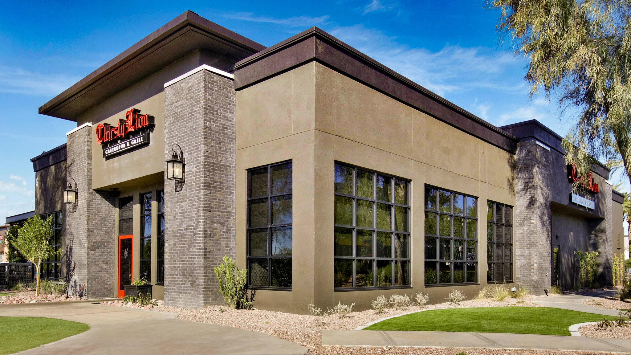 Exterior view of Thirsty Lion Gastropub & Grill with its modern design and large windows under a bright blue sky.