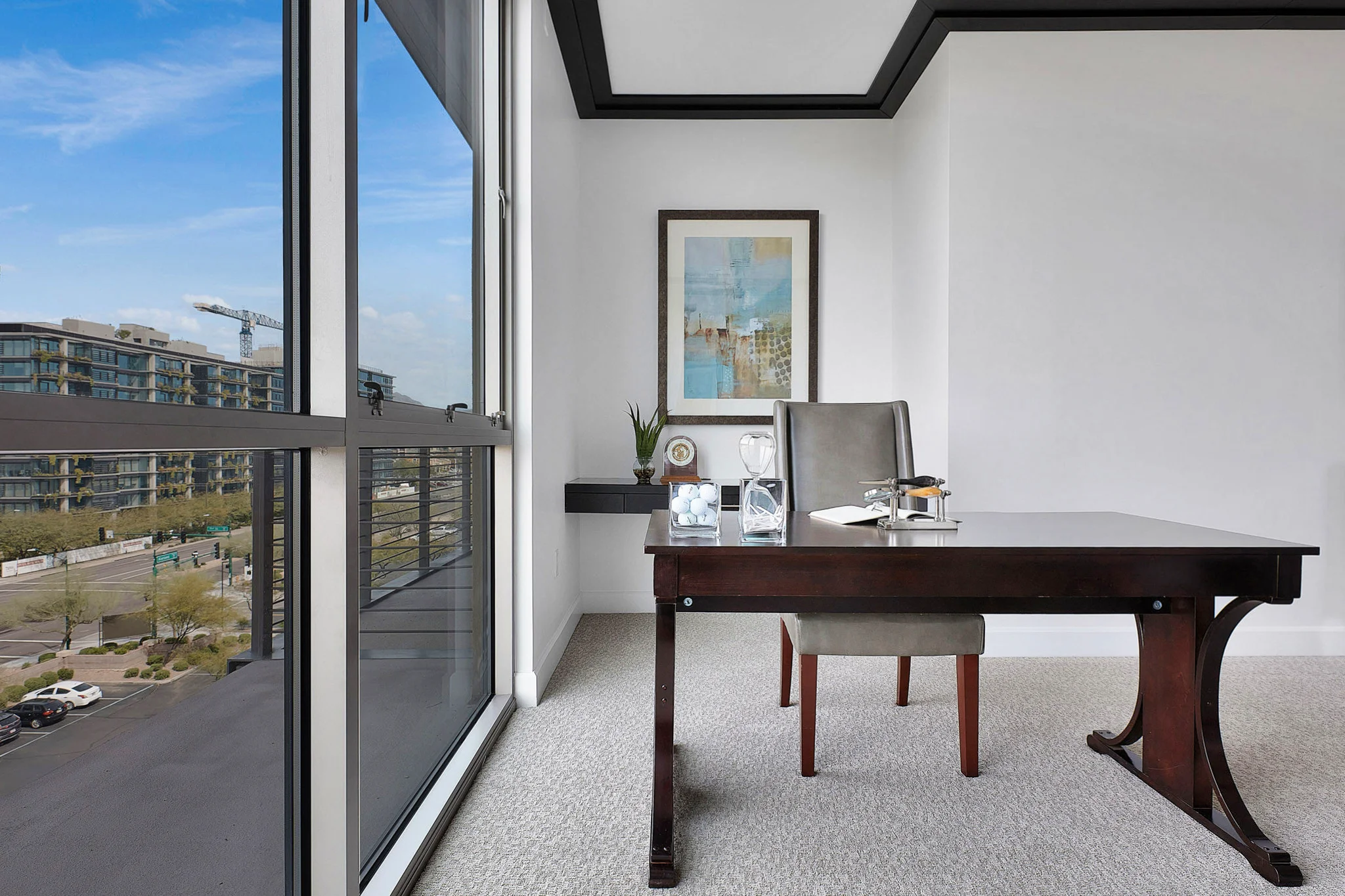 Modern office space with a sleek wooden desk, leather chair, and large windows overlooking an urban landscape.